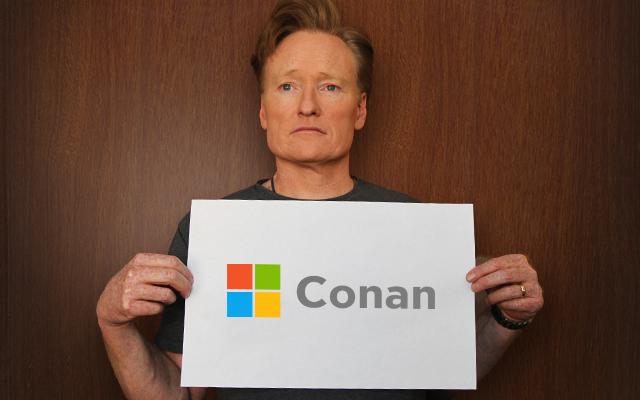 Conan o'brien holds a sign with a redesigned microsoft logo