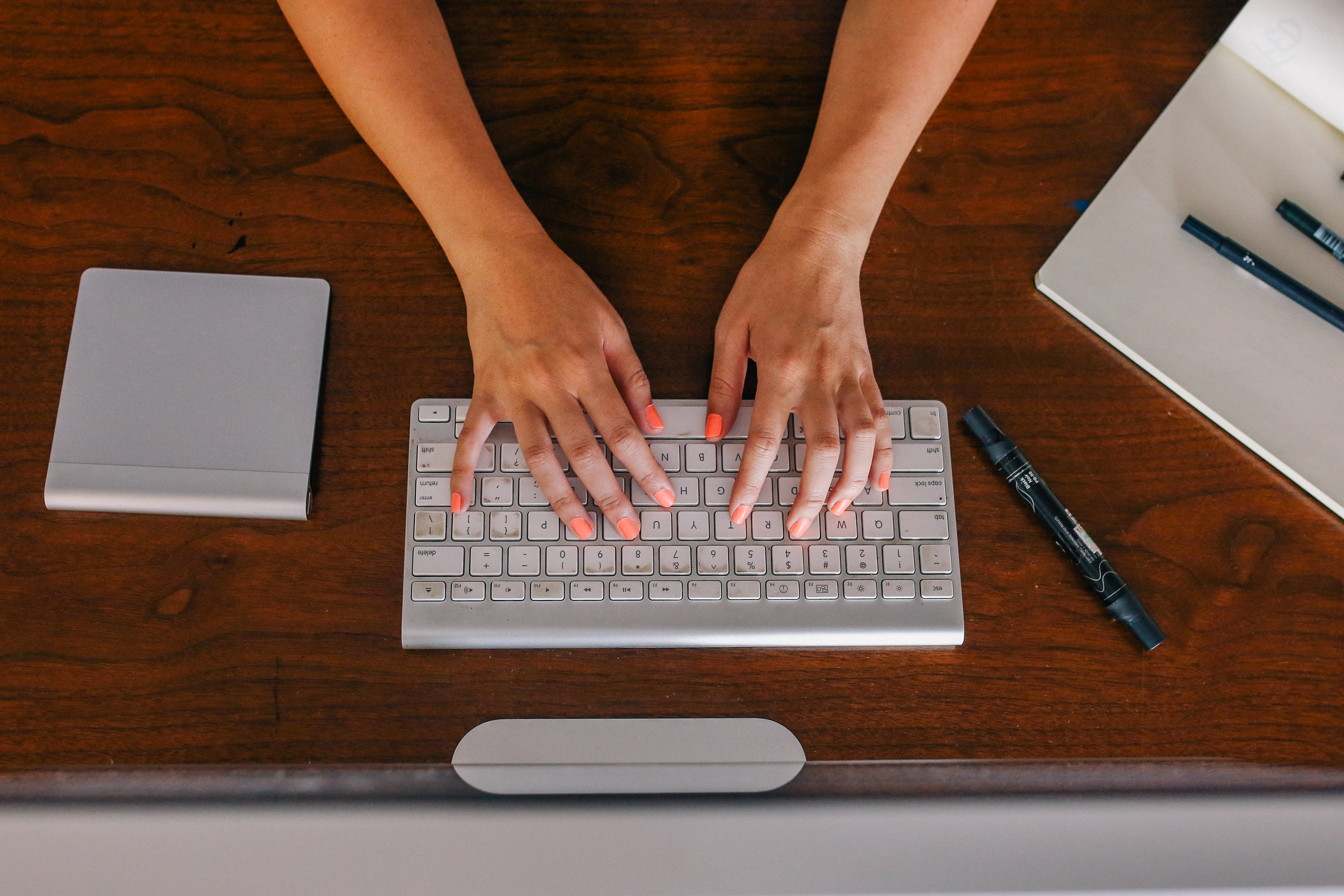 woman with orange fingernails typing